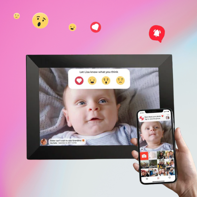 Hand holding a black digital frame displaying baby photo with emoji reactions, smartphone beside showing photo gallery.